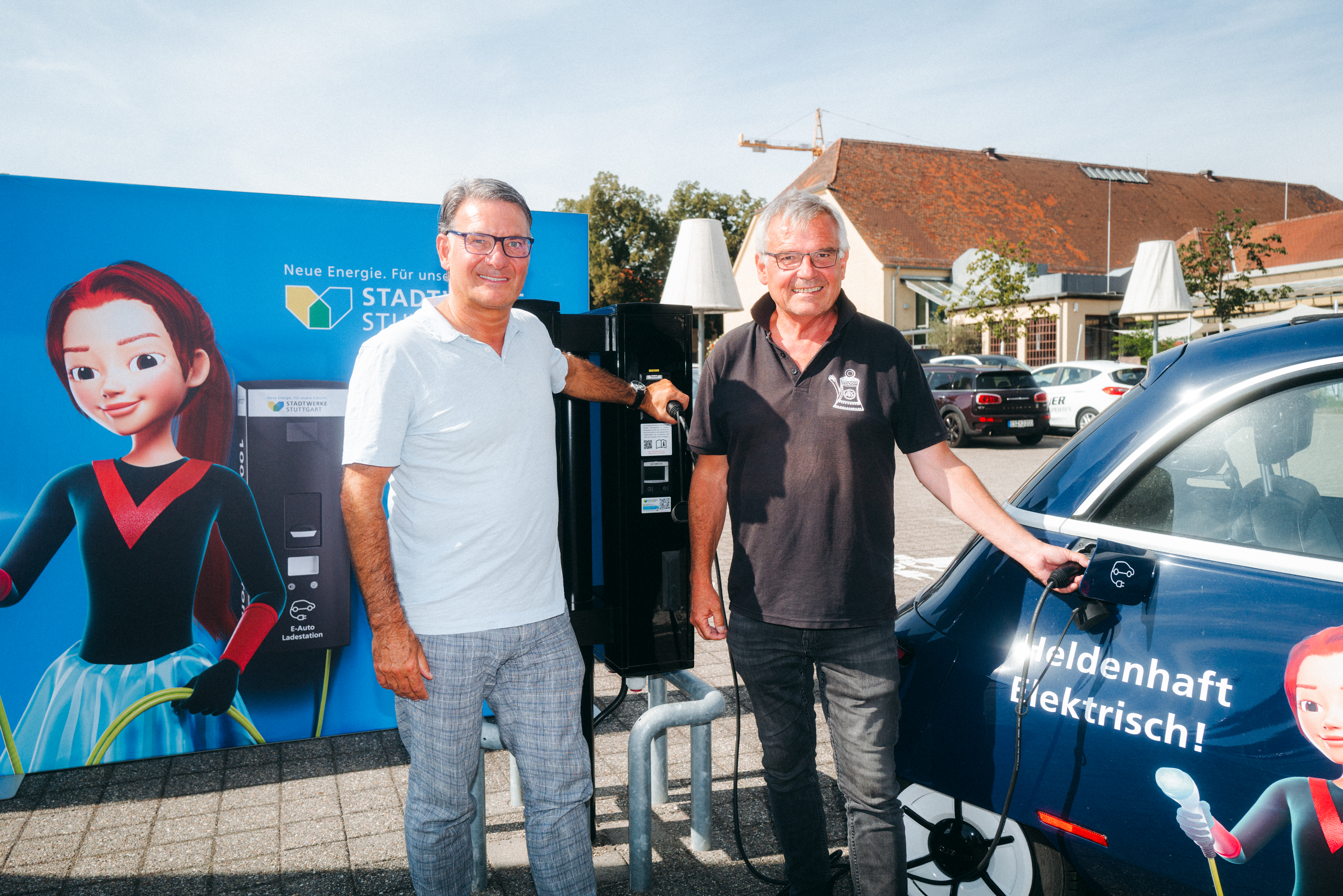 Zwei Männer laden ein blaues E-Auto an schwarzer Ladesäule.